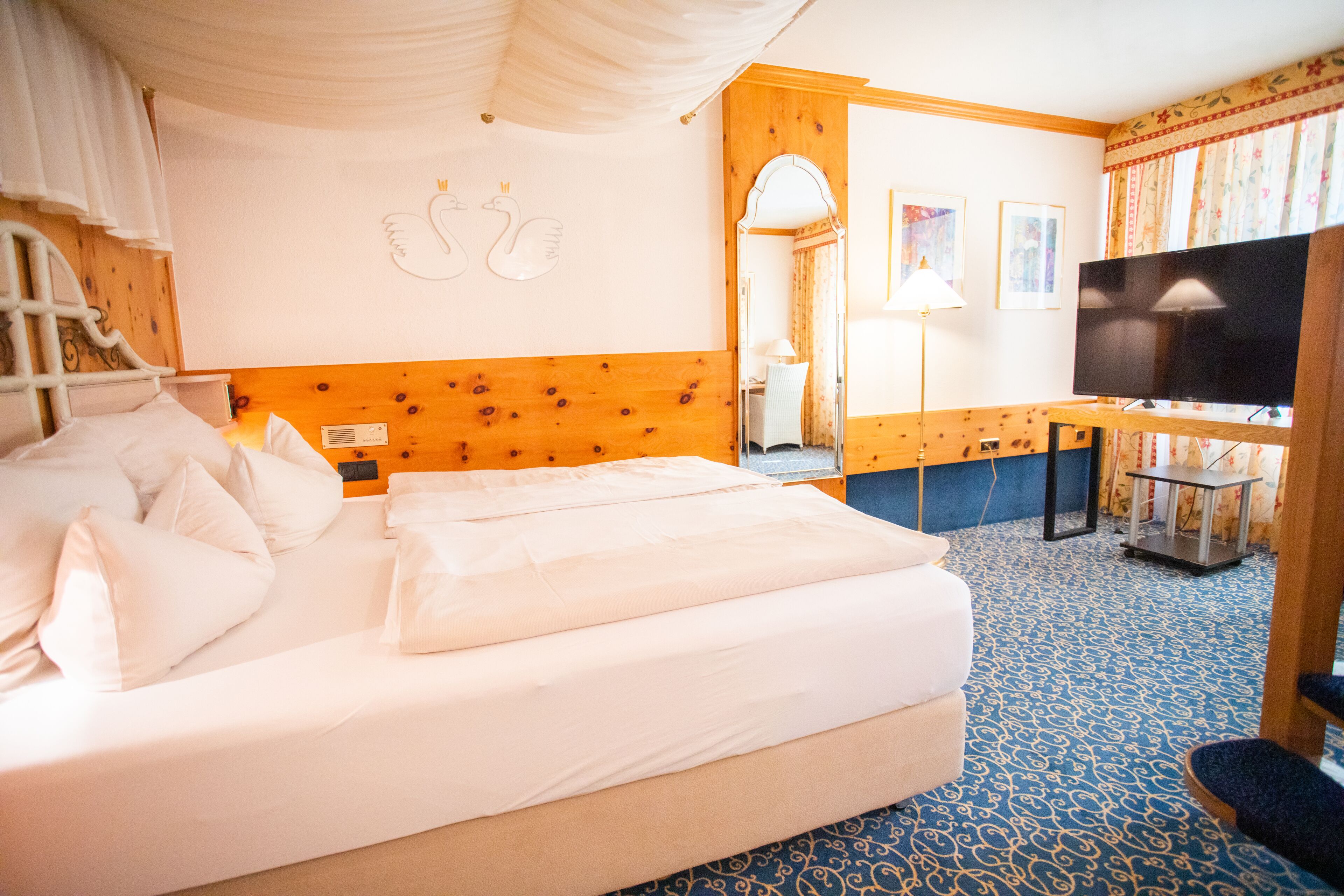 A hotel room with a large bed, a desk with a television, and a mirror.
