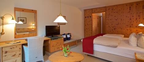 Une chambre d’hôtel avec un bureau en bois, une télévision, un lit et une petite table ronde agrémentée d’un vase de fleurs.