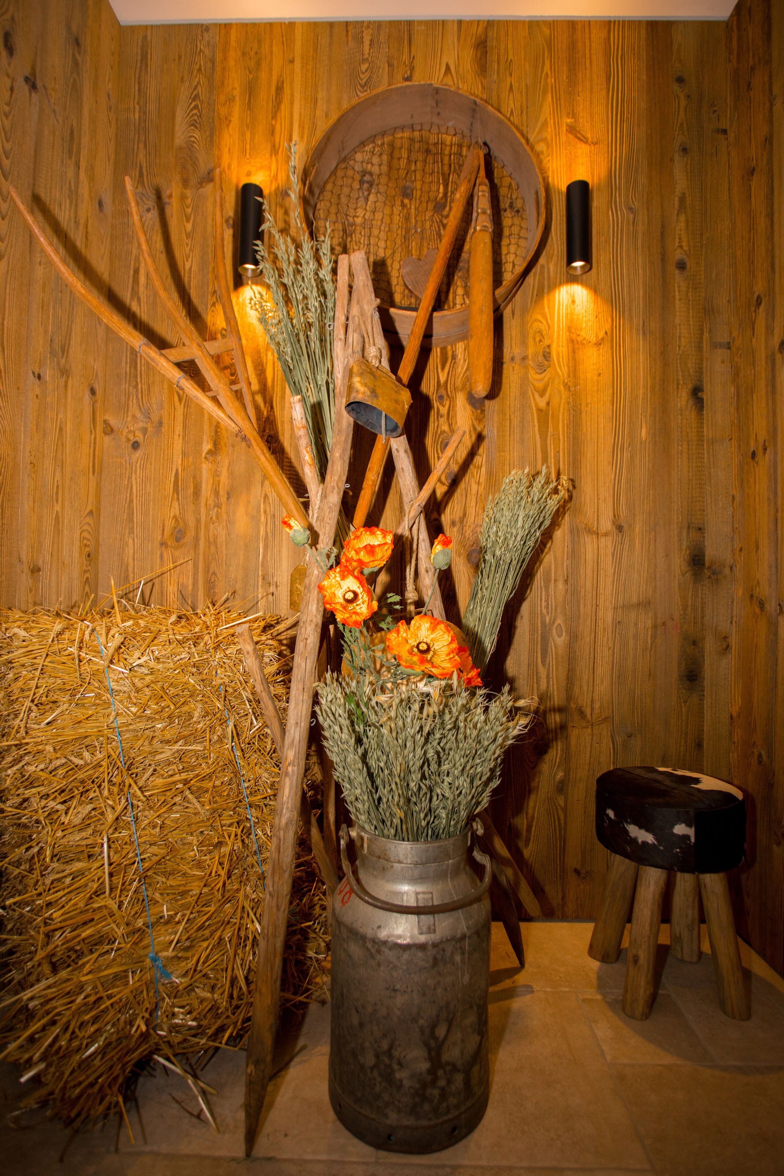 Un intérieur rustique avec un vase en métal contenant des fleurs et des branches séchées, un mur en bois et une botte de foin.