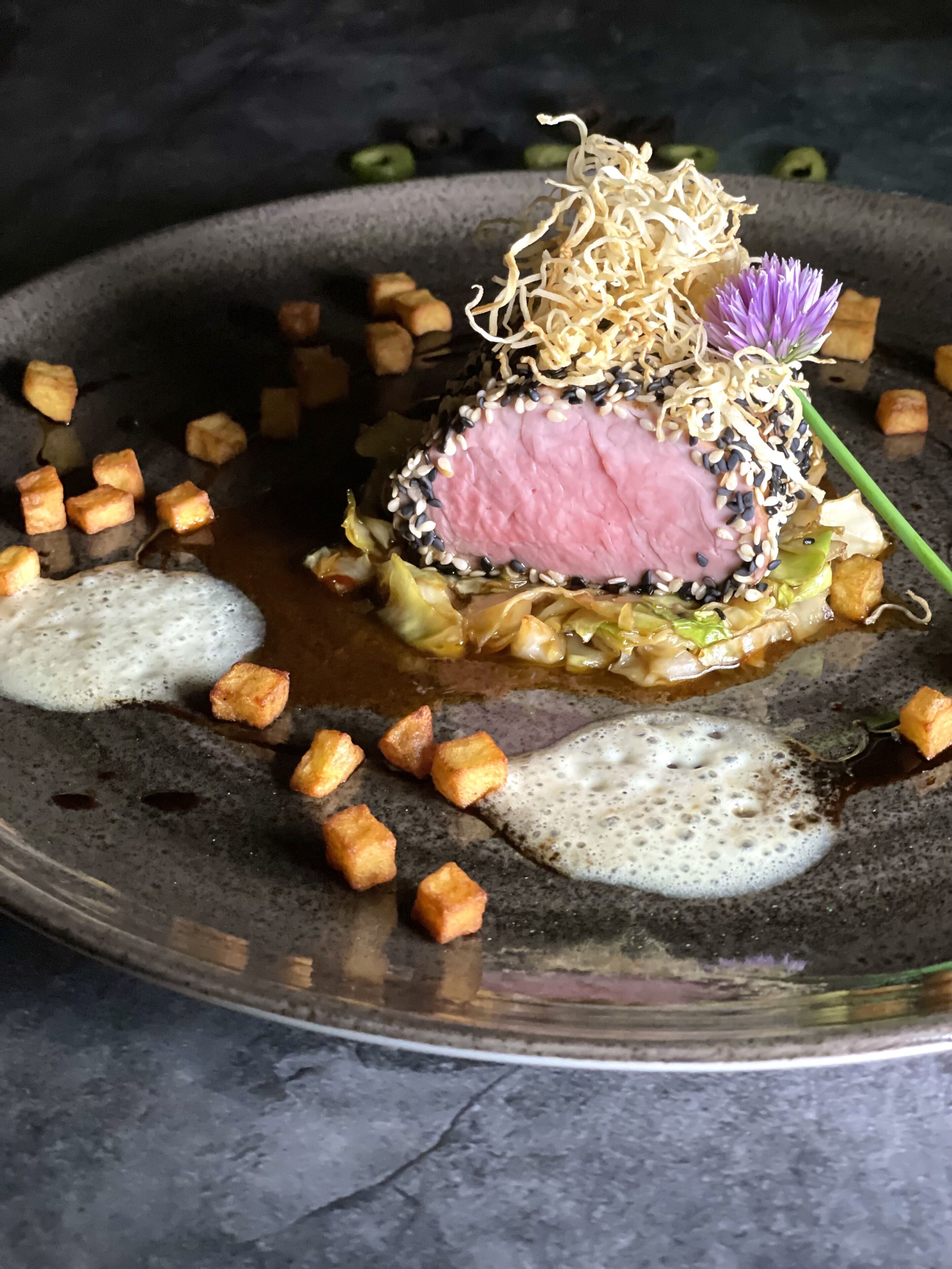 A dish with a pink center, surrounded by various garnishes and small cubes.