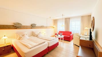 Ein Hotelzimmer mit einem großen Bett, einem roten Sofa, einem kleinen Tisch mit Flasche und Gläsern sowie einem Schreibtisch mit Lampe.