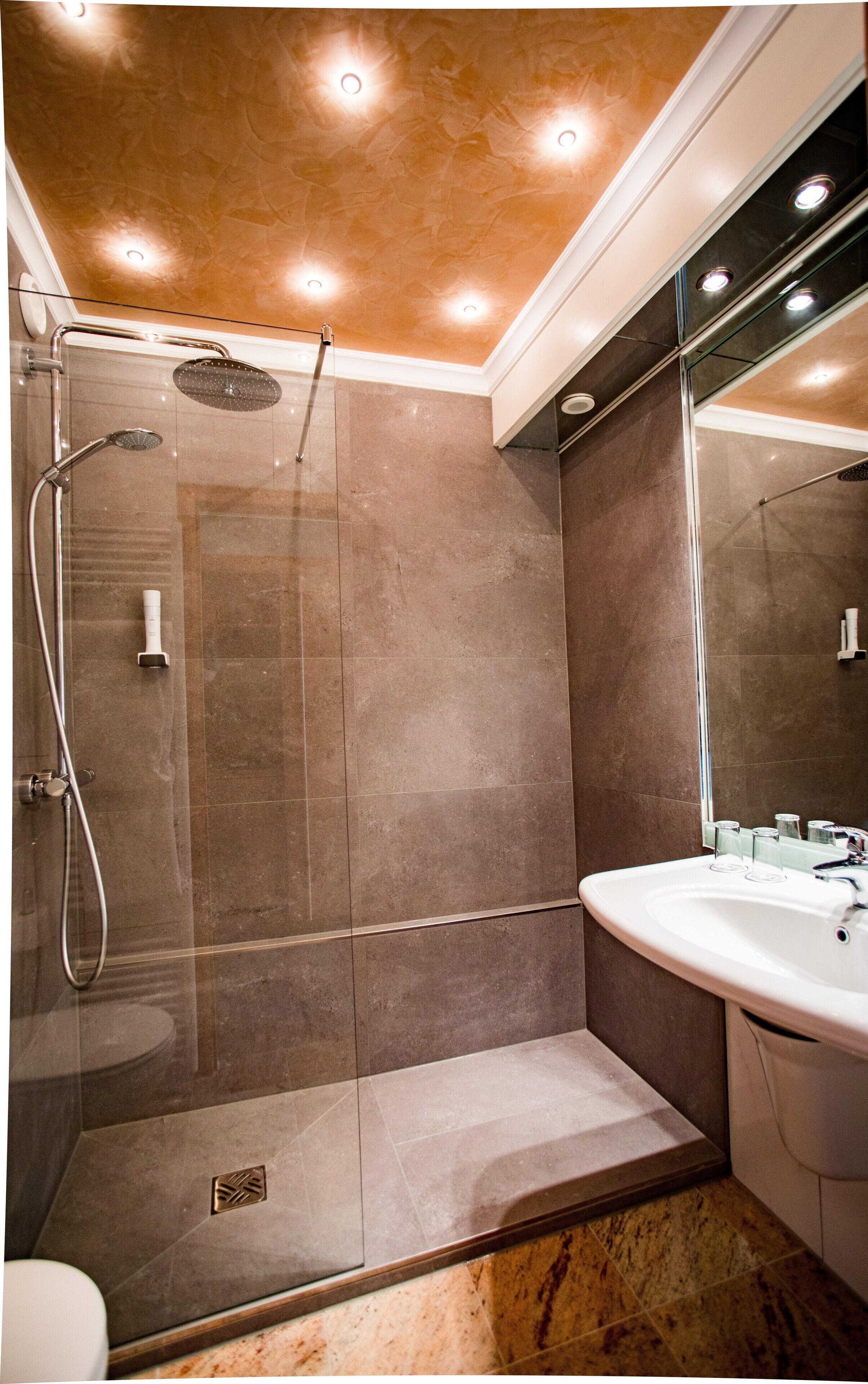 Un baño moderno con ducha de vidrio, un lavabo blanco y suelo de mármol.