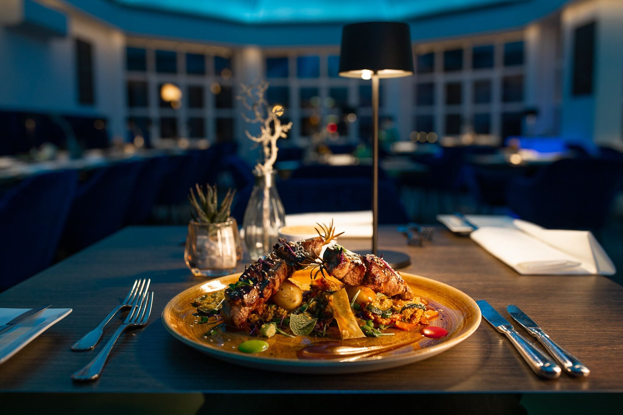 A dining table with a plate of food, cutlery, and a lamp.