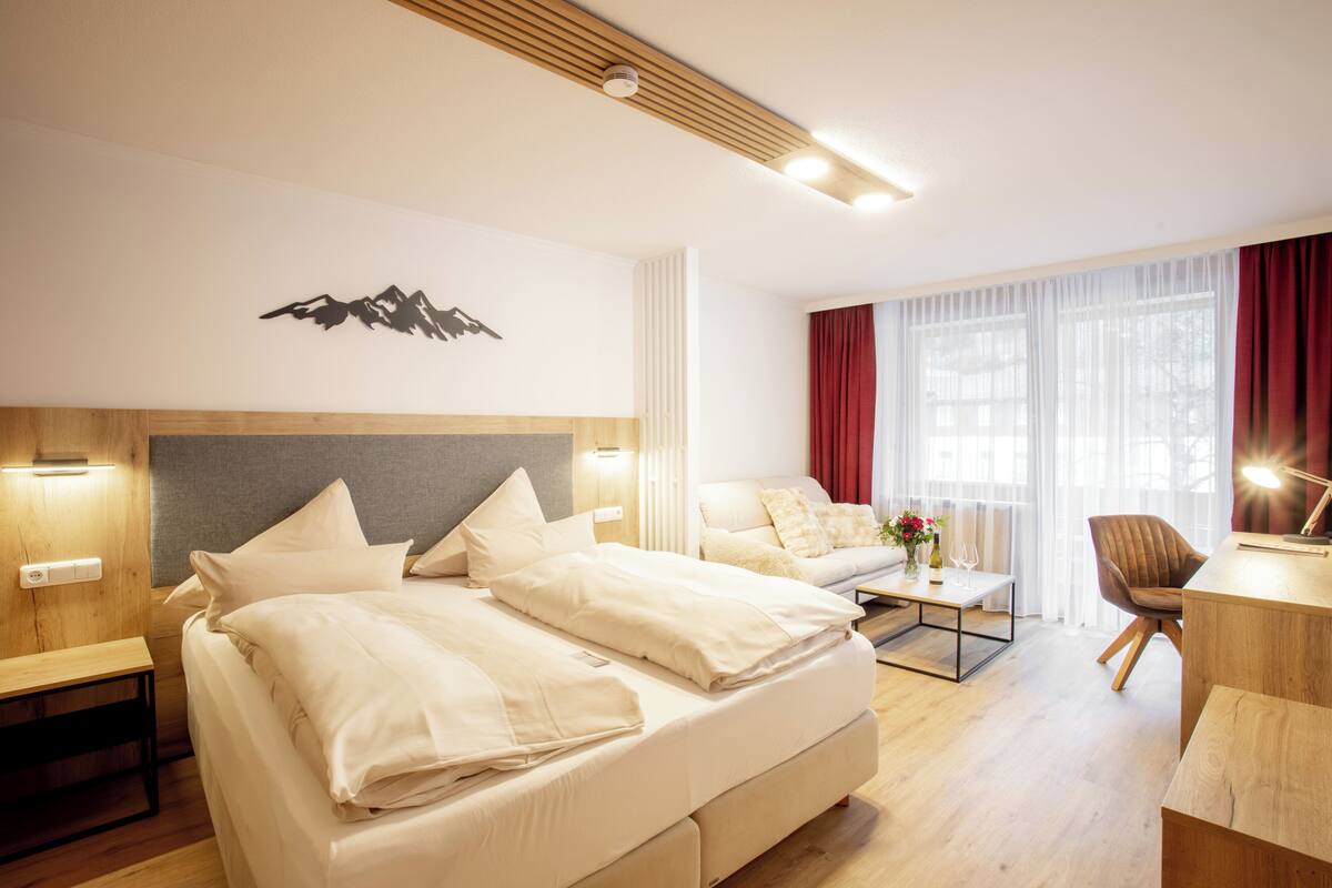 Une chambre d’hôtel moderne avec un grand lit, un canapé, un bureau et une vue sur l’extérieur.
