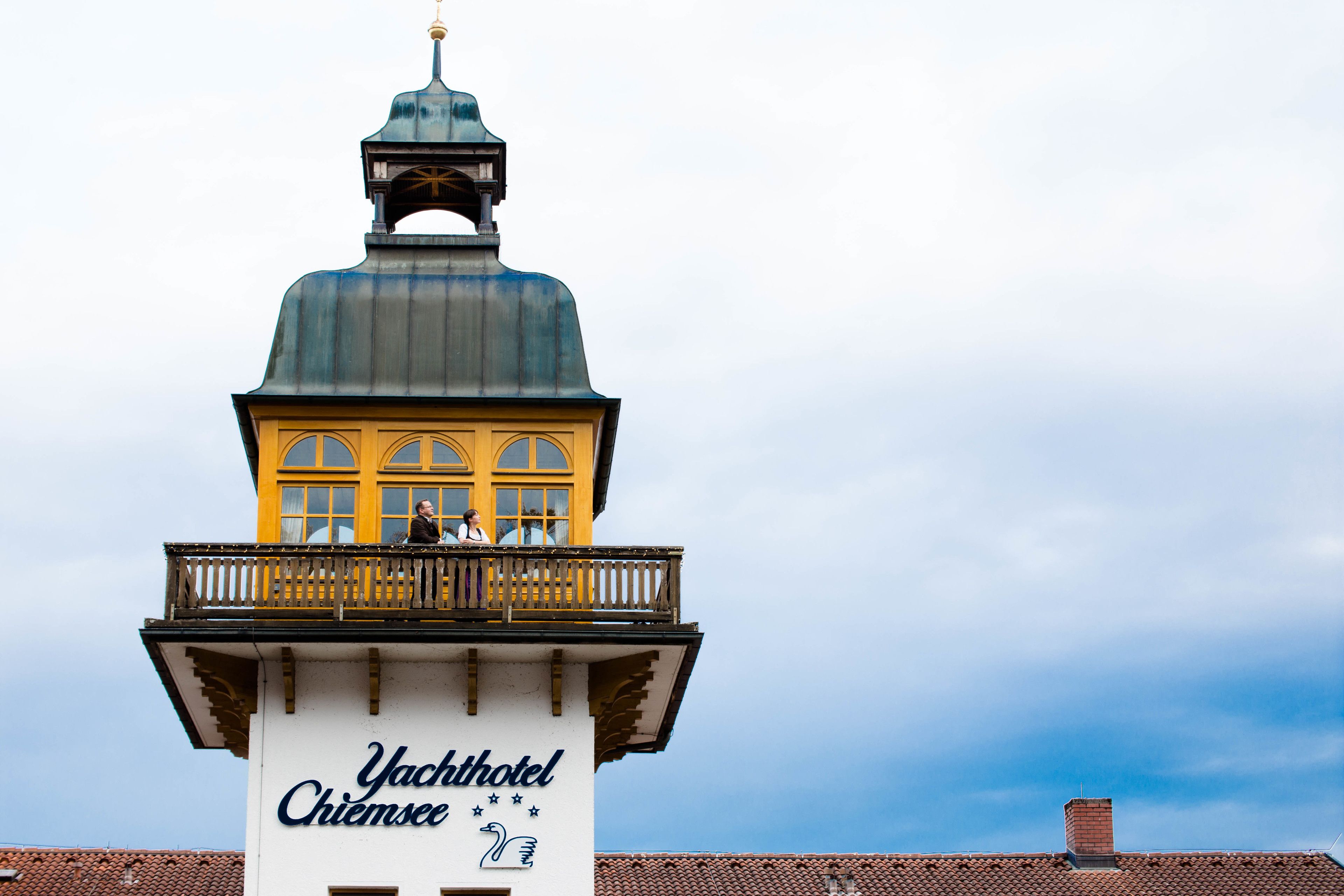 Un edificio con un cartel que dice "Yachthotel Chiemsee" y un balcón con dos personas.