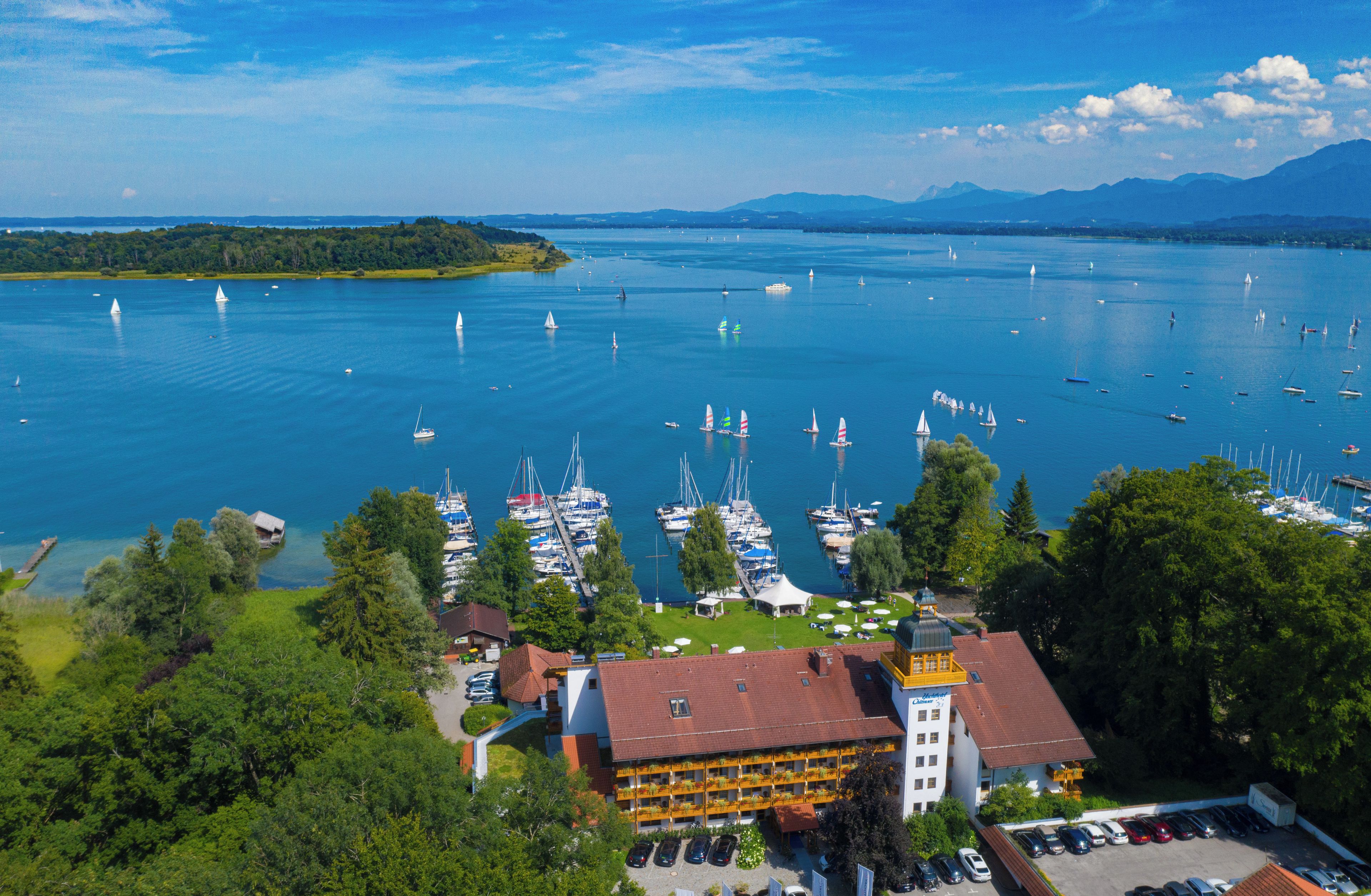 Un port de plaisance avec des bateaux, un bâtiment doté d’un toit rouge et une zone boisée.