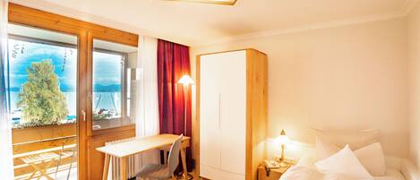 A hotel room with a bed, a desk, a chair, a wardrobe, and a view of the outdoors.