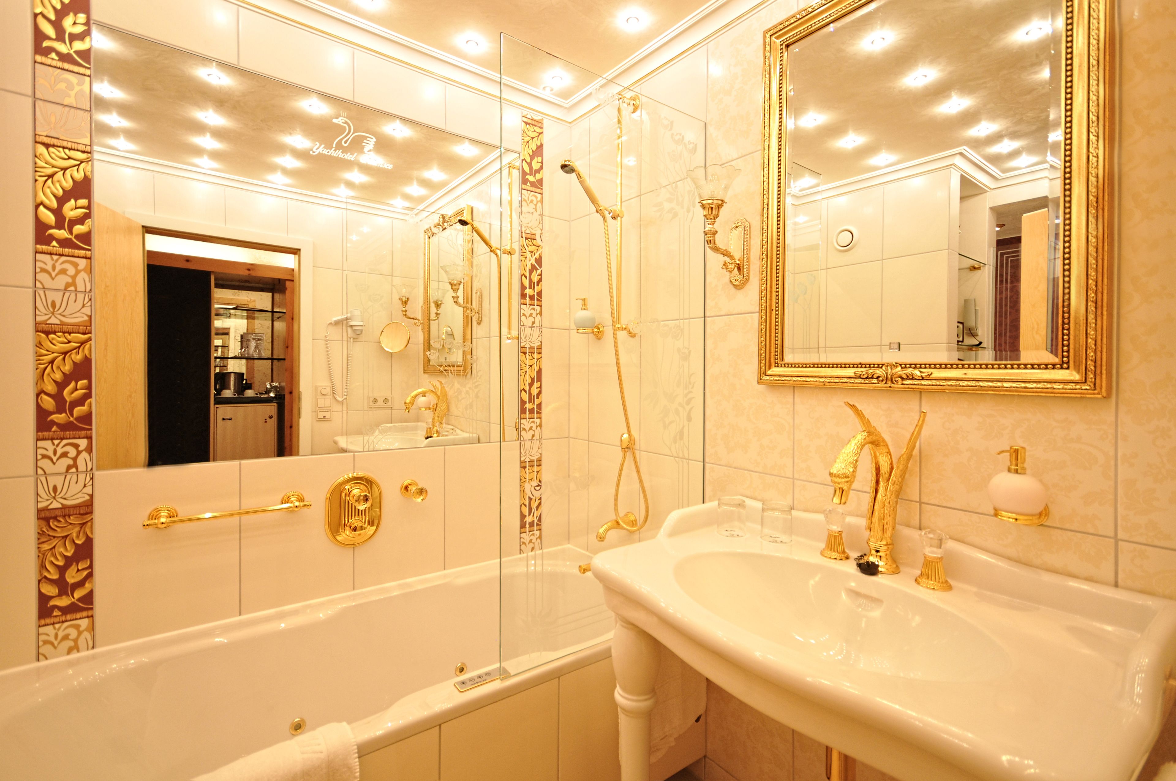 A luxurious bathroom with a large bathtub, a sink with gold fixtures, and a mirror with a gold frame.