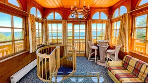 Een houten chalet met grote ramen, een spiltrap en een eethoek met rieten meubels.