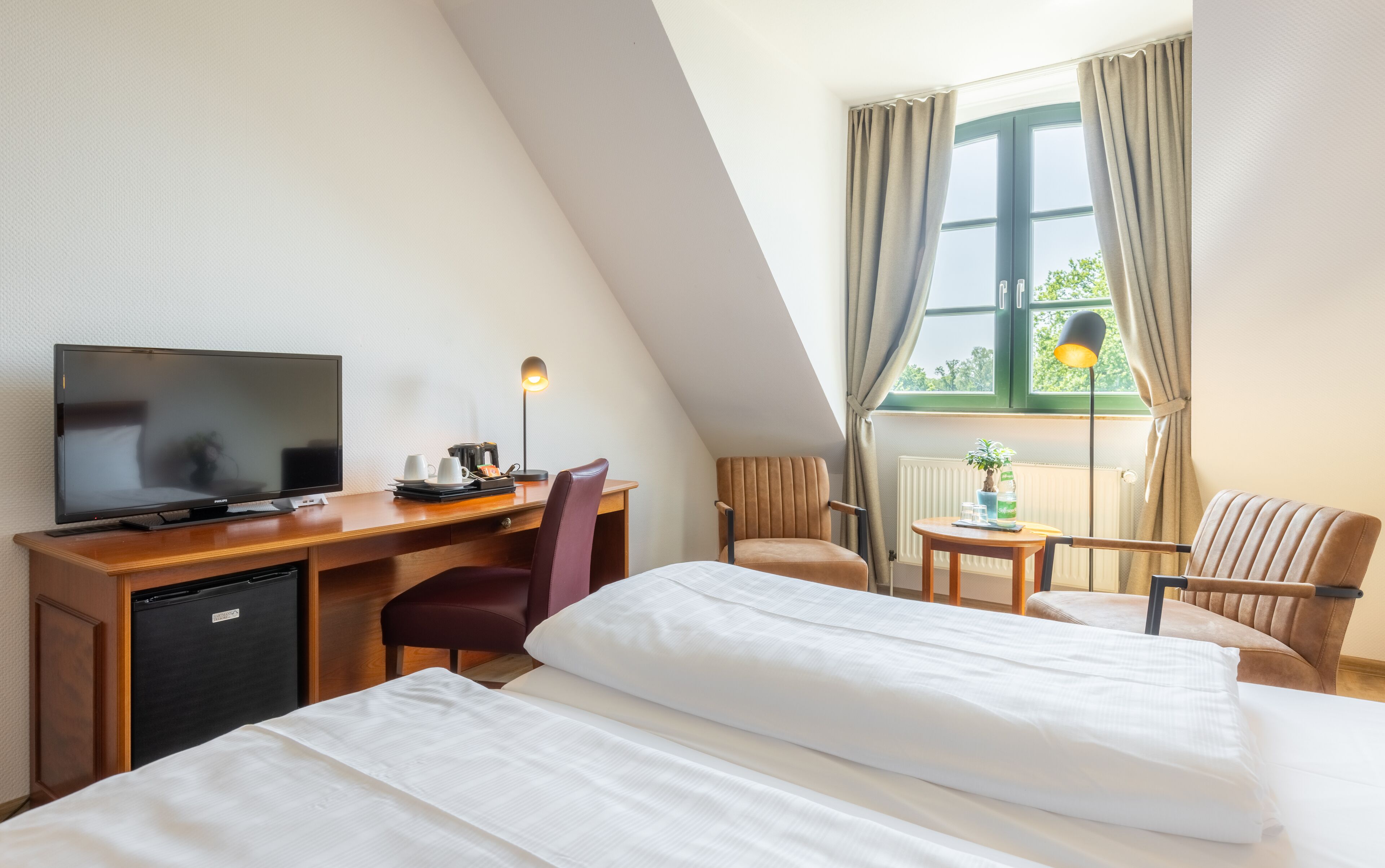 Een hotelkamer met een bed, bureau, televisie en een raam met gordijnen.