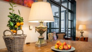 A wooden table with a woven basket containing oranges, a lamp, and a plate of apples. - Hotel Ohlenhoff (Norderstedt)