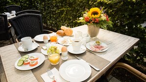 A breakfast table set outdoors with plates of food, a vase of flowers, and a cup of coffee. - Hotel Ohlenhoff (Norderstedt)