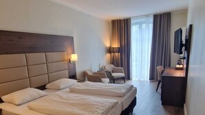 A hotel room with a large bed, a desk, two chairs, a TV, and a window with curtains. - Hotel Ohlenhoff (Norderstedt)