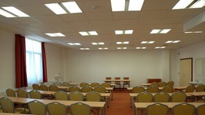 Une salle de classe avec des rangées de bureaux et de chaises, un tableau blanc et une fenêtre ornée de rideaux rouges.