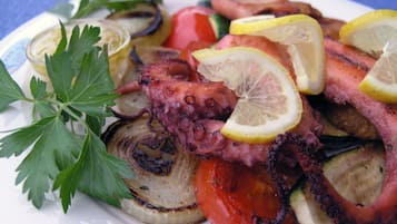 Une assiette de poulpe grillé, accompagné de légumes et de tranches de citron.