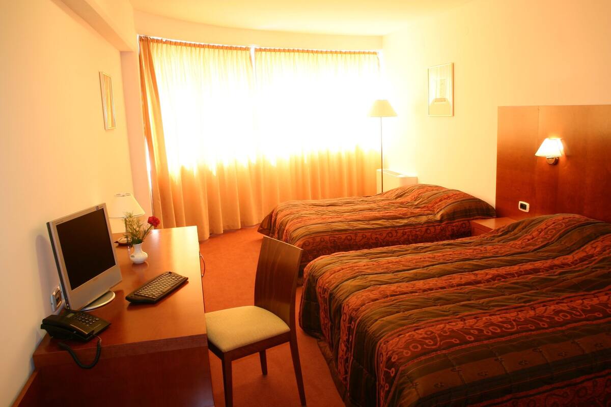 Een hotelkamer met twee bedden, een bureau met een computer, een stoel en een lamp.