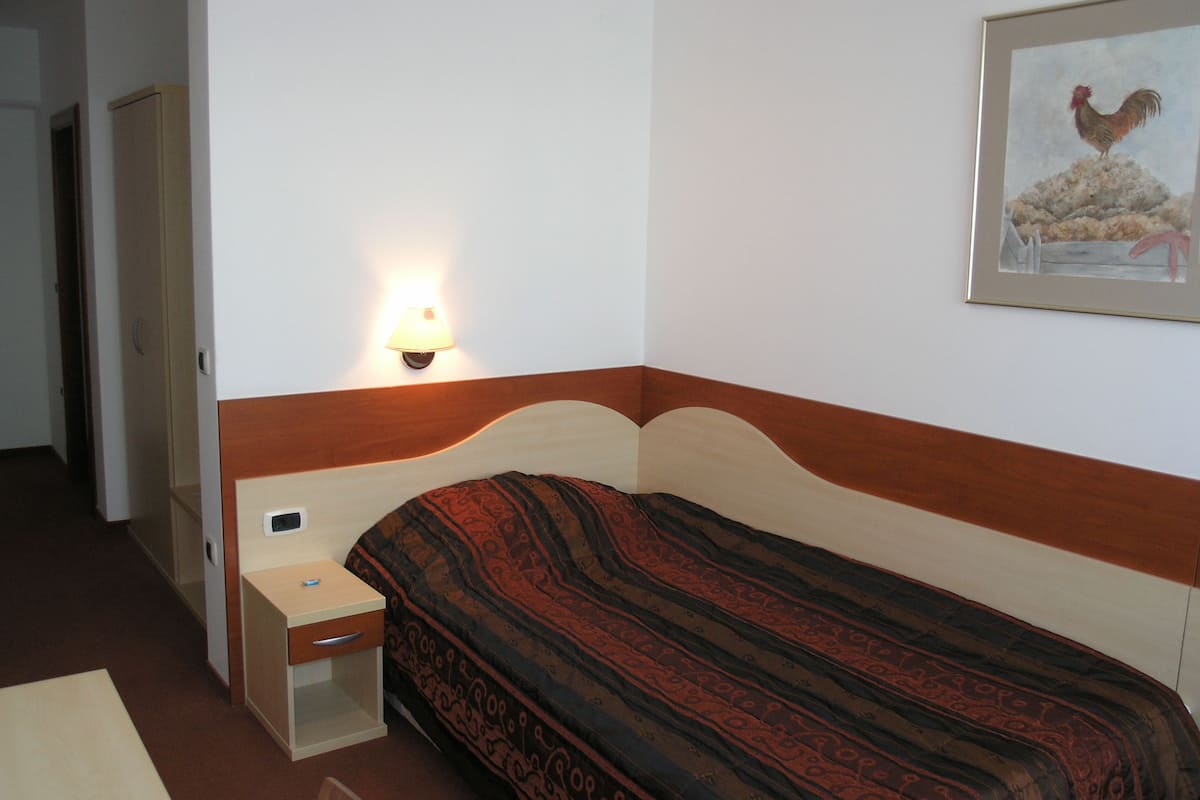 Een enkel bed met een beddengoed met een patroon, een nachtkastje met een lamp en een lijst met een afbeelding aan de muur.