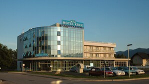 Un hôtel moderne avec une façade en verre, une enseigne bien visible et un parking où sont garées plusieurs voitures.
