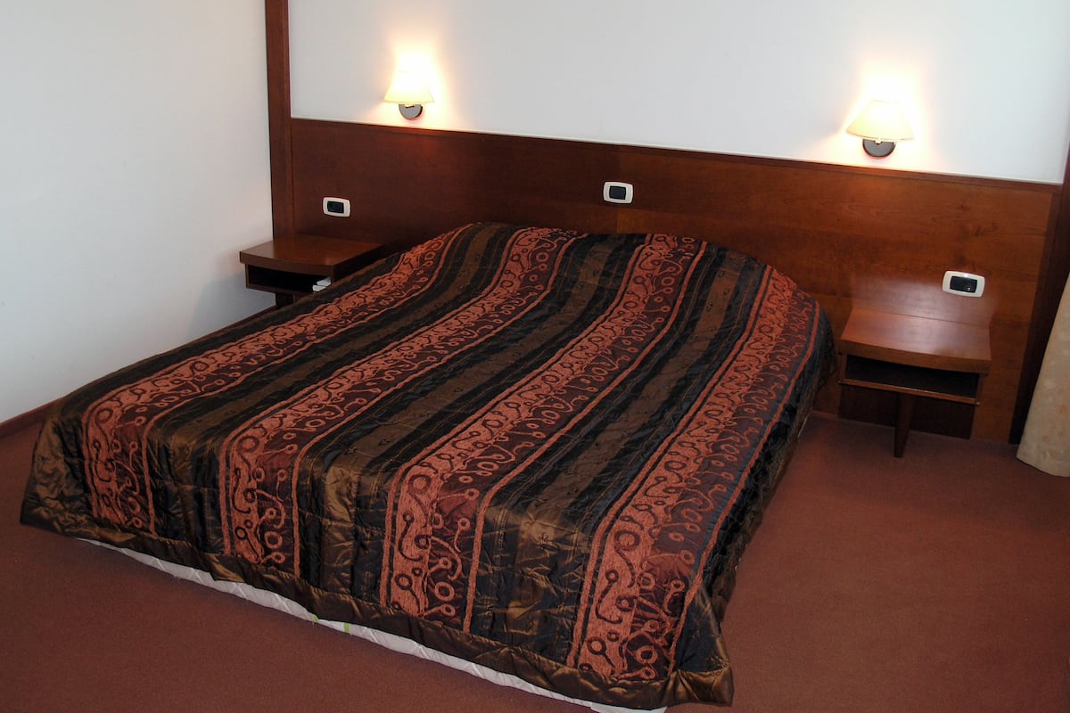 Een net opgemaakt bed met een beddekleed met patroon, twee nachtkastjes met lampen en een hoofdbord.