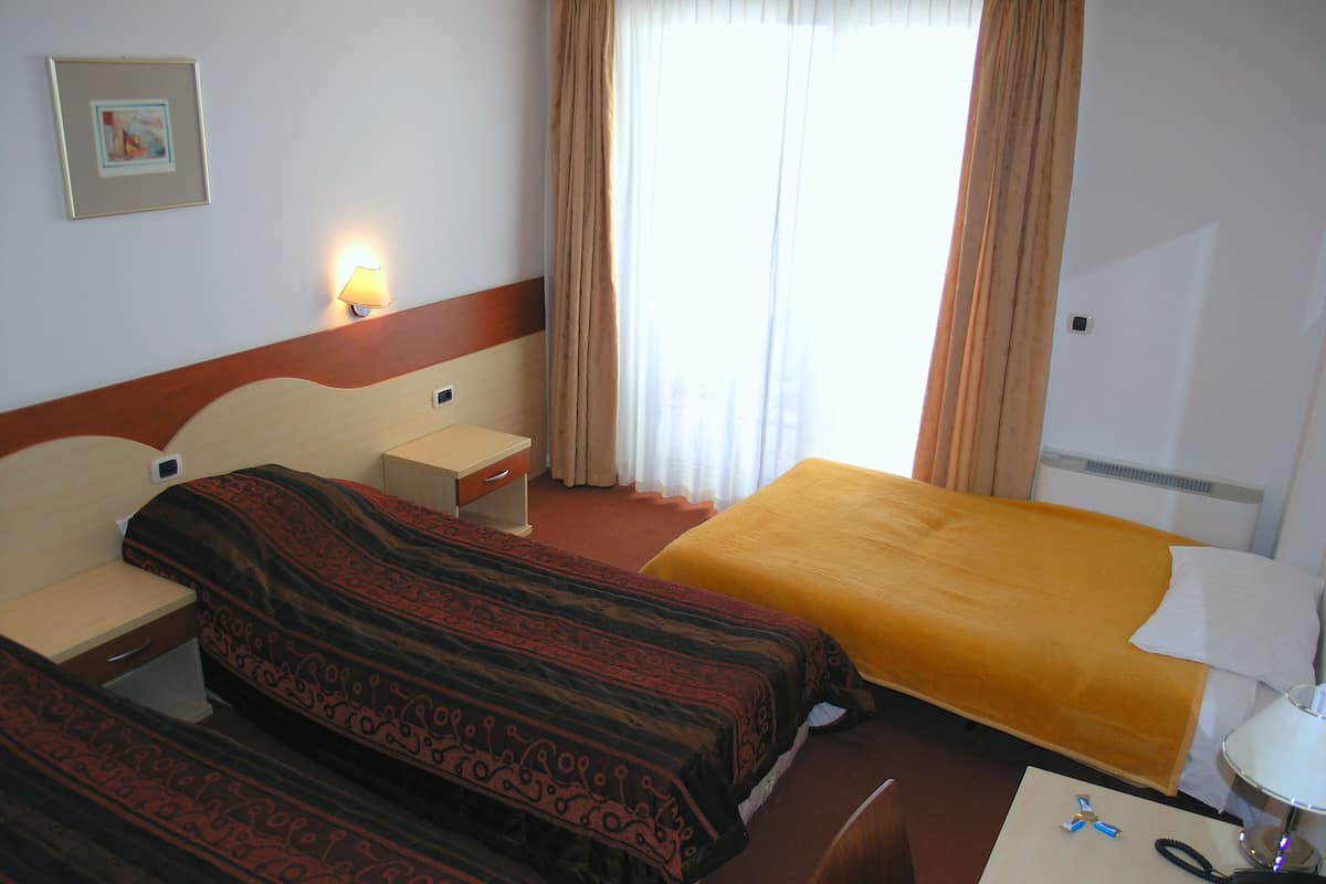Een hotelkamer met twee bedden, een bureau, een stoel, een lamp en een raam met gordijnen.