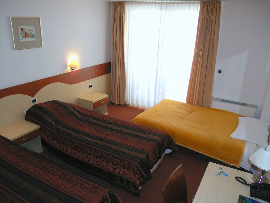 A hotel room with two beds, a desk, a chair, a lamp, and a window with curtains.