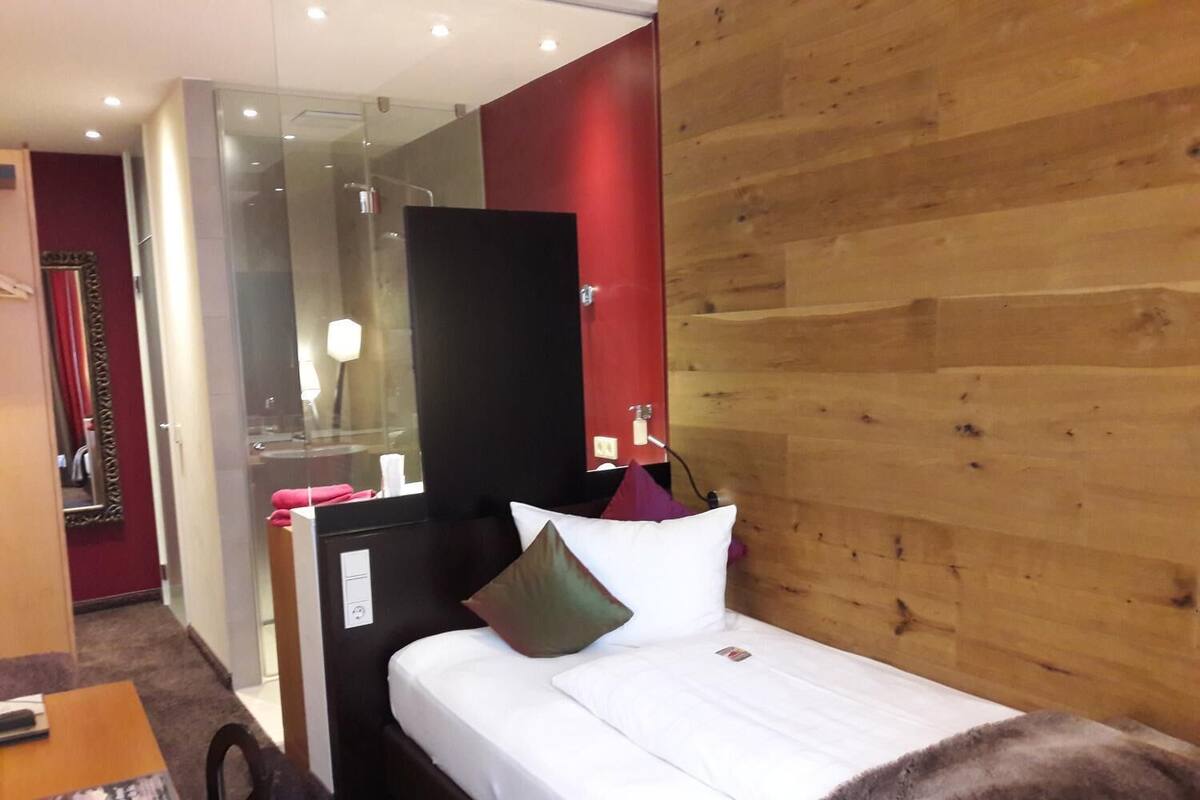 Quarto de hotel com cama, cabeceira de madeira, espelho e uma mesinha de centro com uma revista.