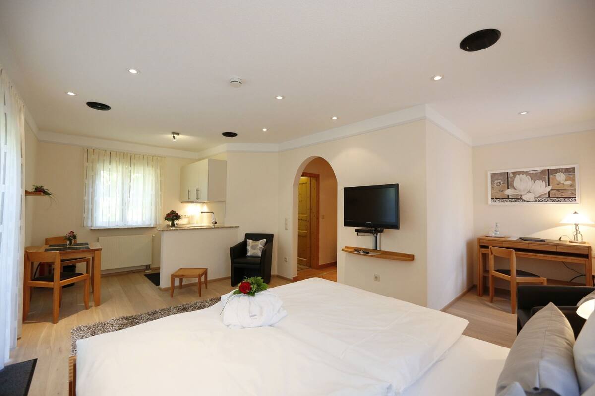 A hotel room with a large bed, a desk, a chair, a television, and a small table with a lamp.