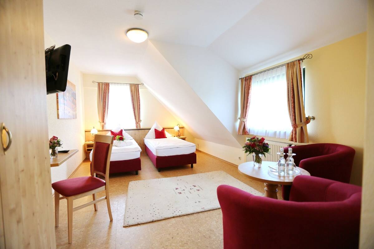 A hotel room with two beds, a desk, a chair, a dining table with chairs, and a TV mounted on the wall.