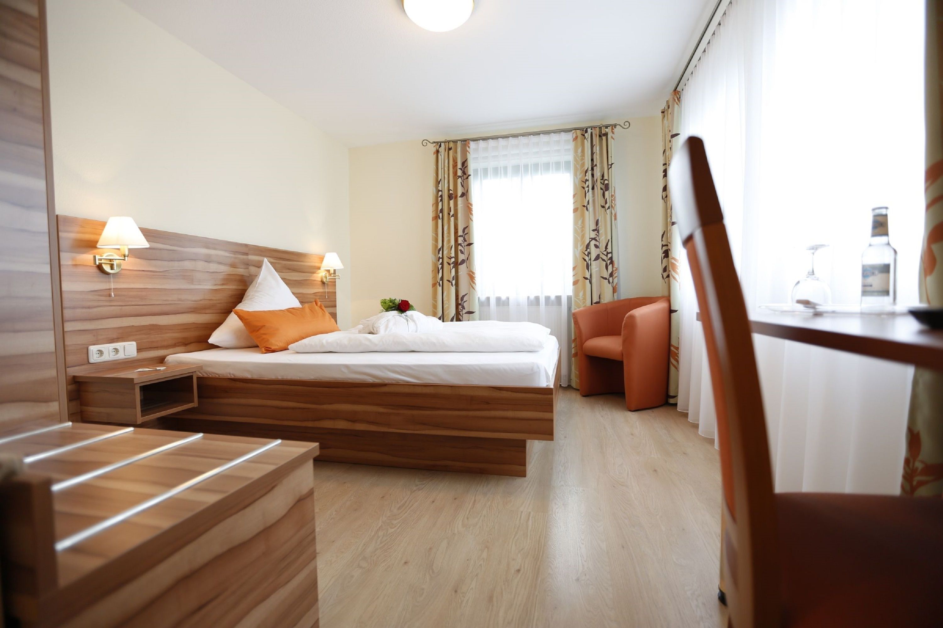 A hotel room with a wooden bed, two bedside lamps, a small table with a bottle, and a chair.