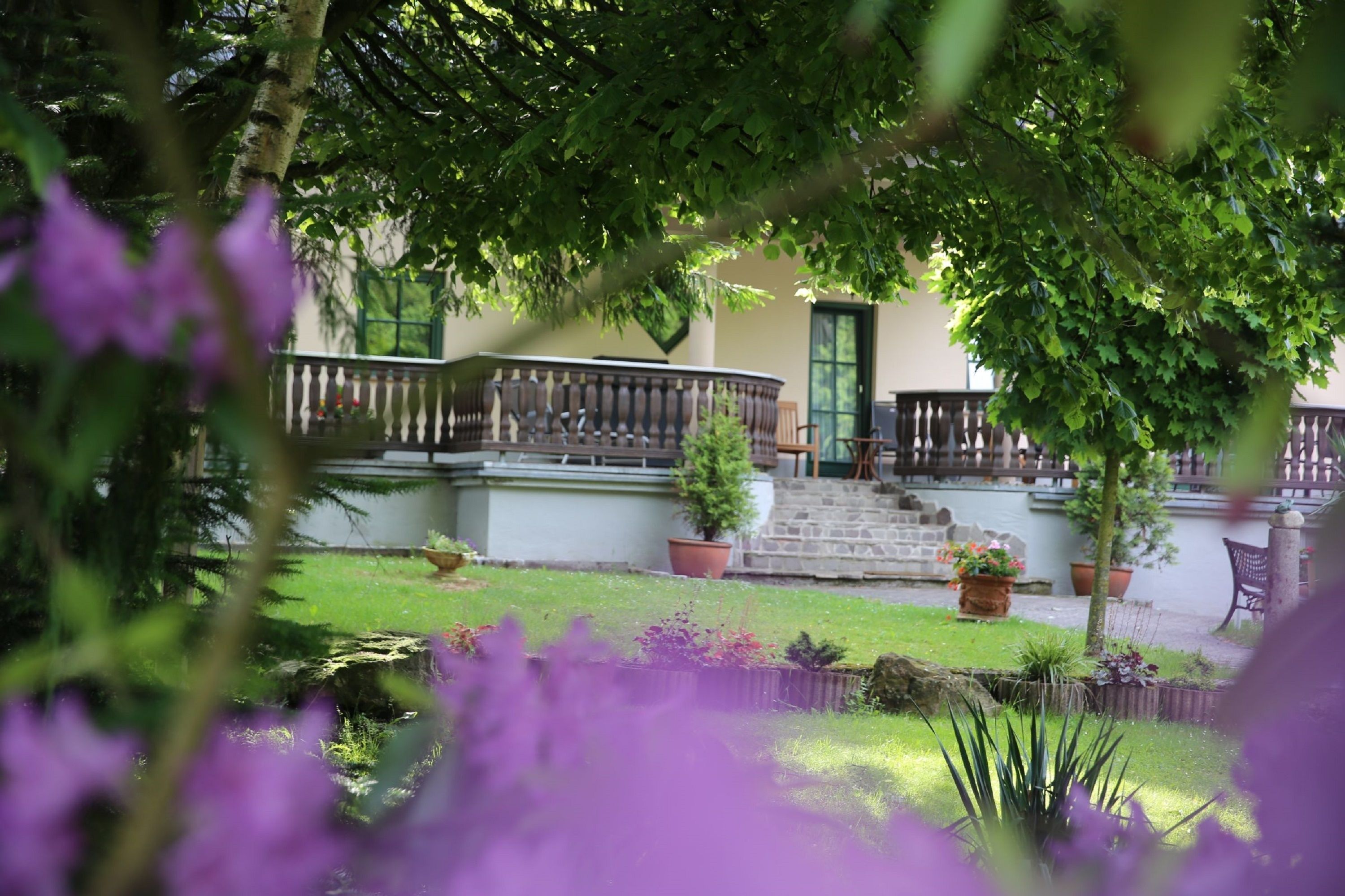 Un jardín con un camino de piedra que lleva a un edificio con una puerta verde. Hay plantas en macetas y un banco en el jardín.