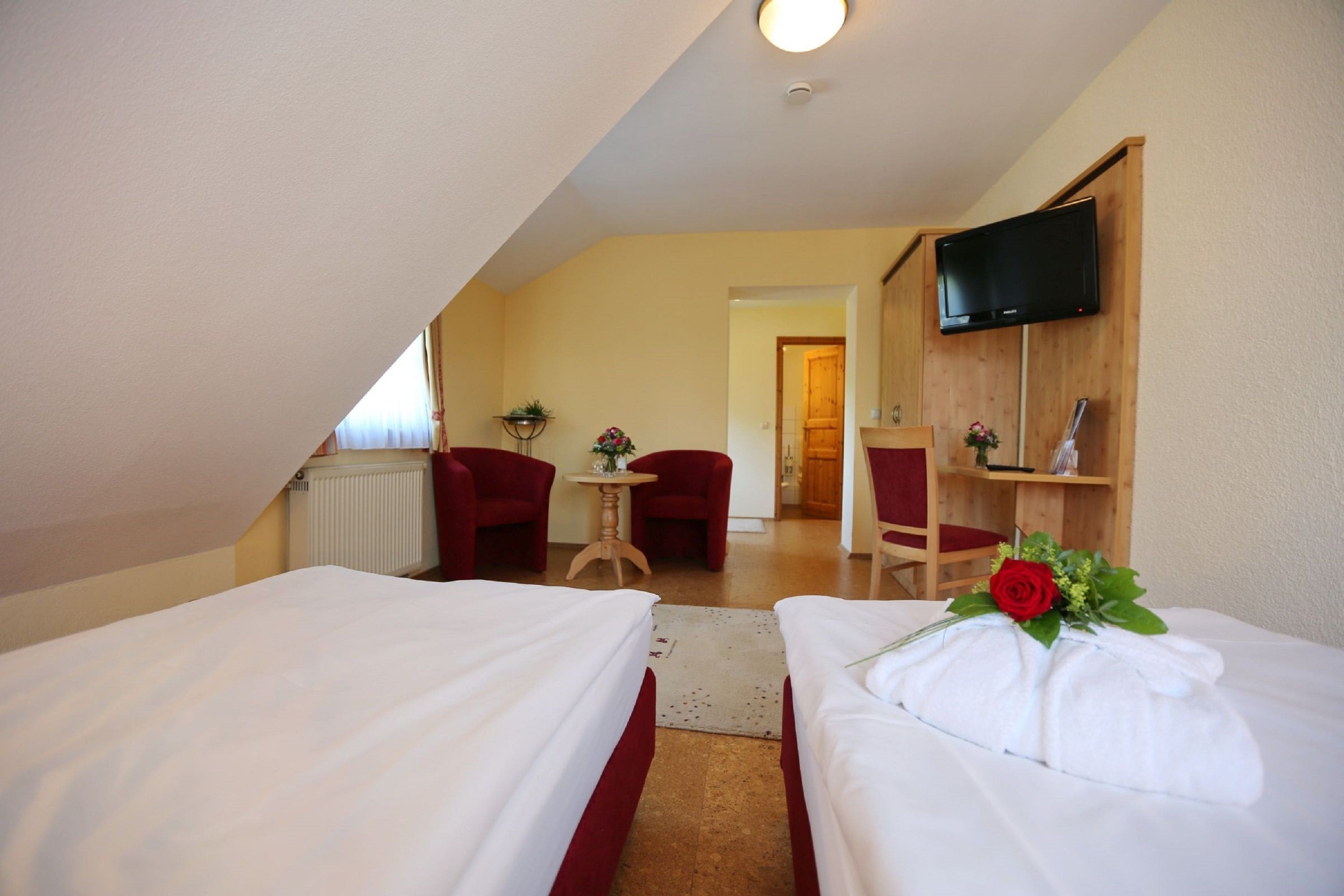 A hotel room with two beds, a TV, a wooden cabinet, and a small table with a flower arrangement.