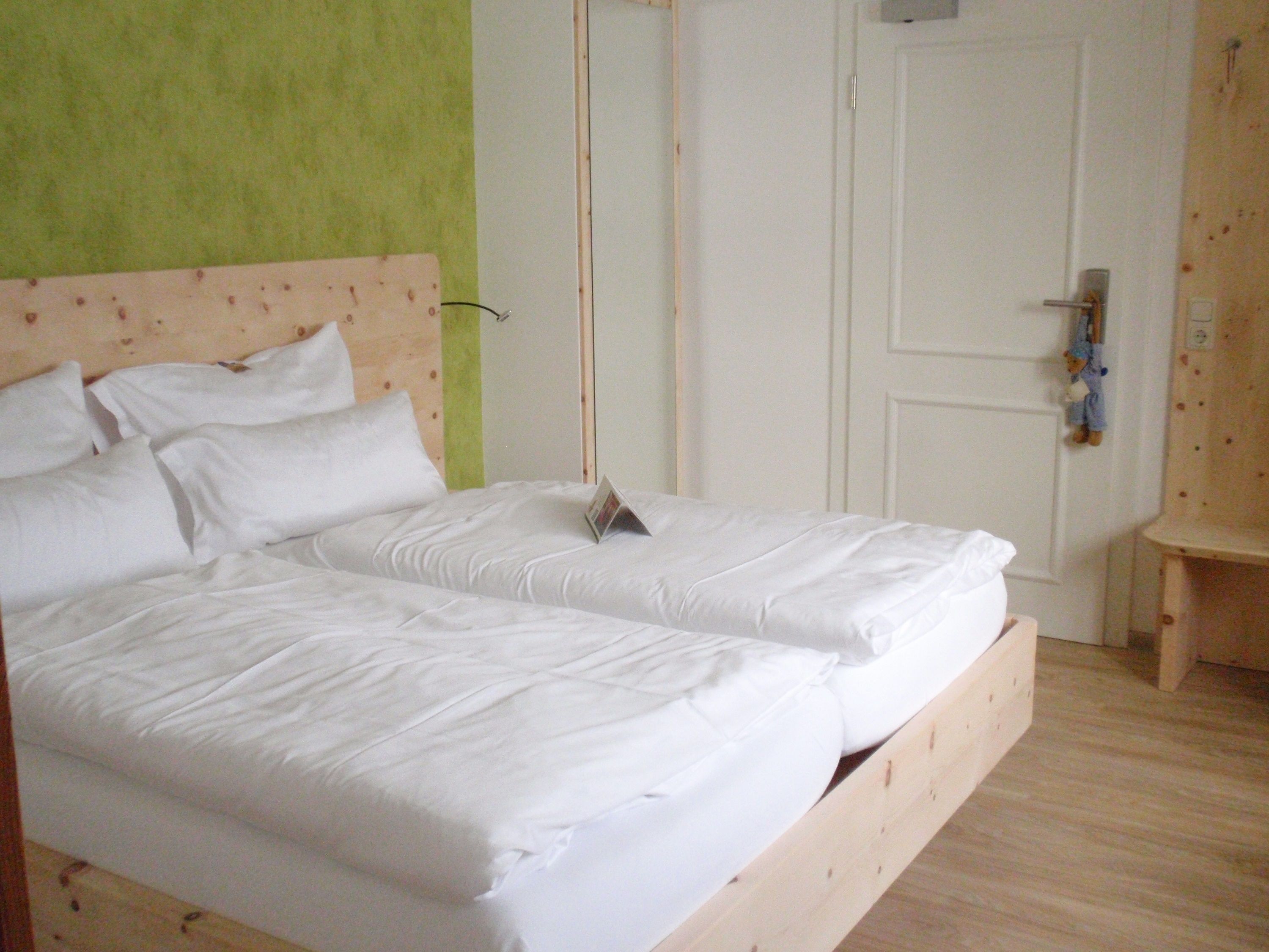 Cama doble con ropa blanca en una habitación con pared verde y cabecera de madera.