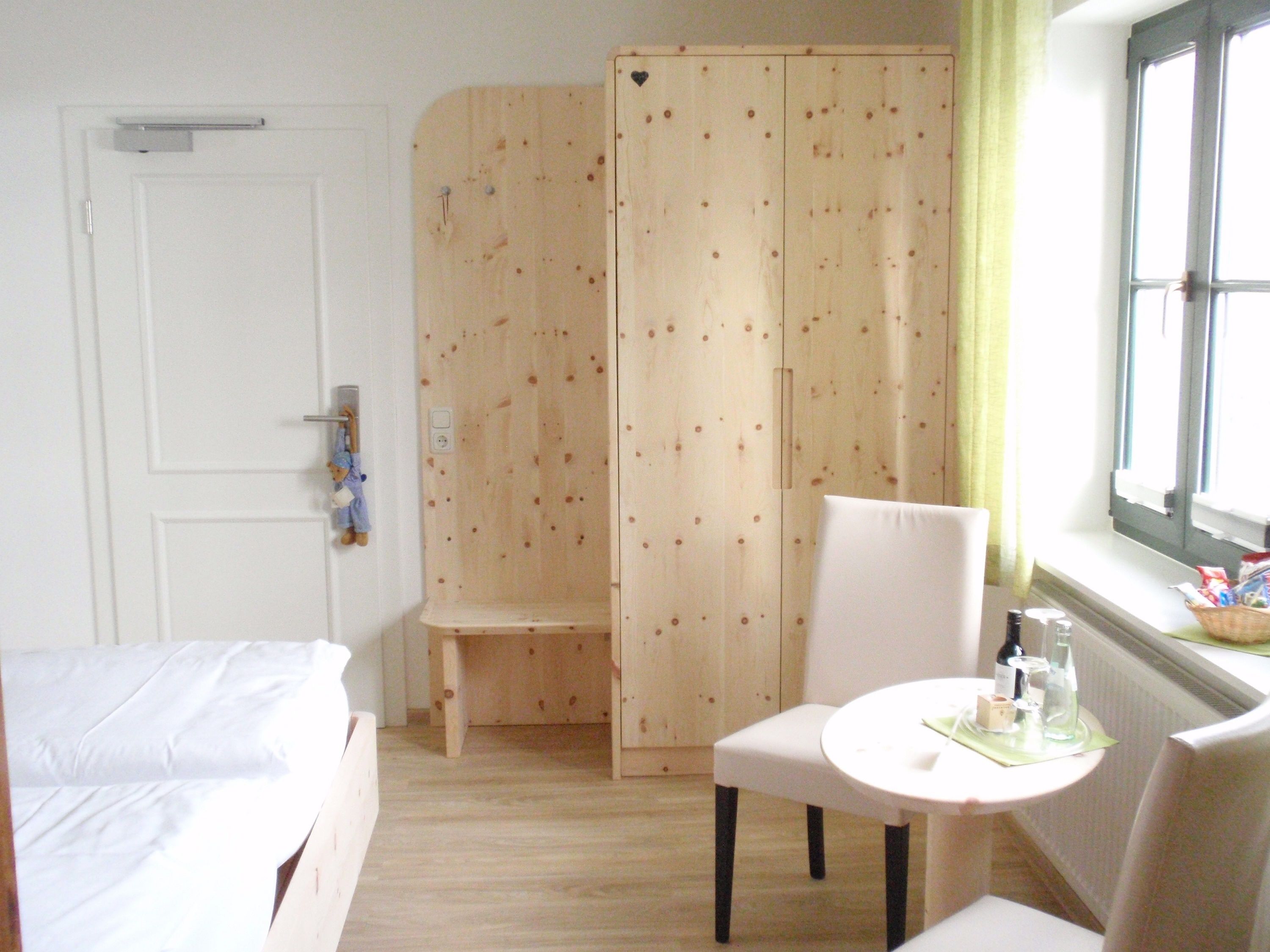 A hotel room with a bed, a small table with bottles, a chair, and a wooden wardrobe.