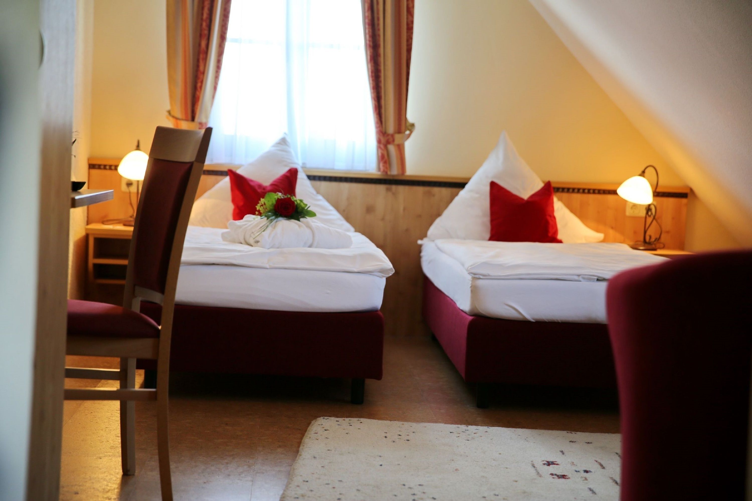 Habitación de hotel con dos camas, cada una con ropa de cama roja y blanca, una mesita y una silla.