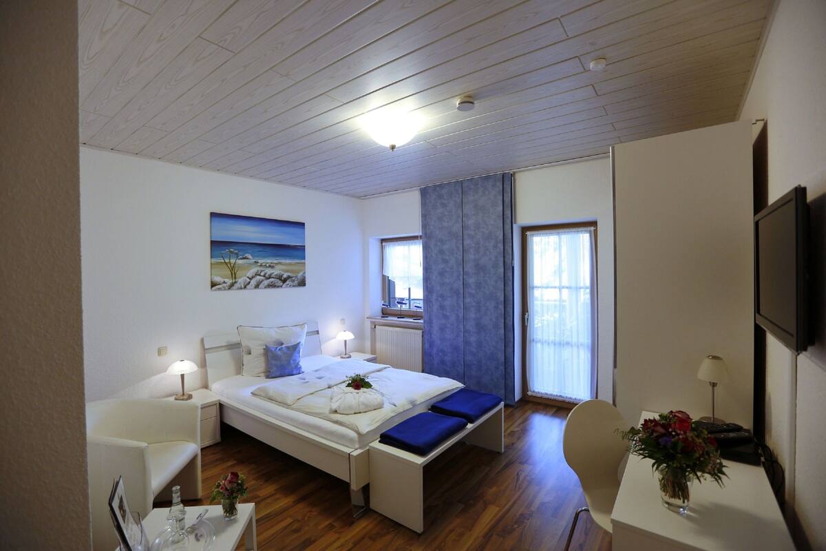 A bedroom with a bed, bedside tables, a desk, a chair, a TV, and a window with curtains.