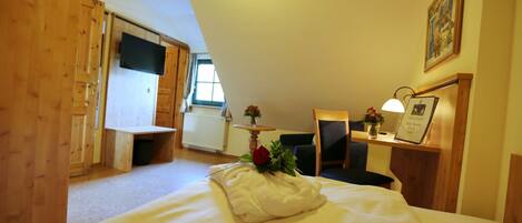 A bedroom with a bed, a desk, a chair, a small table with a vase and a picture frame, and a window.