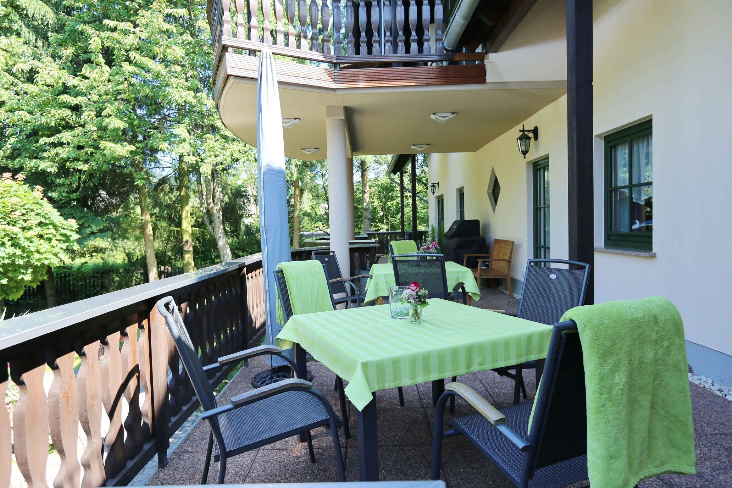 An outdoor patio with a table and chairs, a grill, and a view of trees.