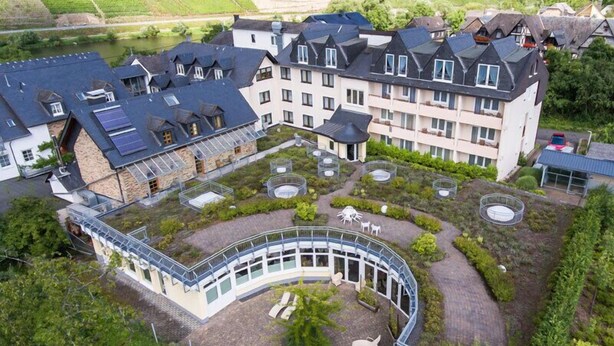 A large hotel with multiple buildings, a central courtyard with seating and a pond, and a surrounding landscaped area. - Hotel Restaurant Pollmanns (Ernst)