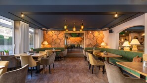 A restaurant with wooden flooring, green upholstered seating, and pendant lighting. - Hotel Restaurant Pollmanns (Ernst)
