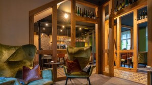 A cozy interior with plush chairs, a bar area with bottles, and a stone wall. - Hotel Restaurant Pollmanns (Ernst)