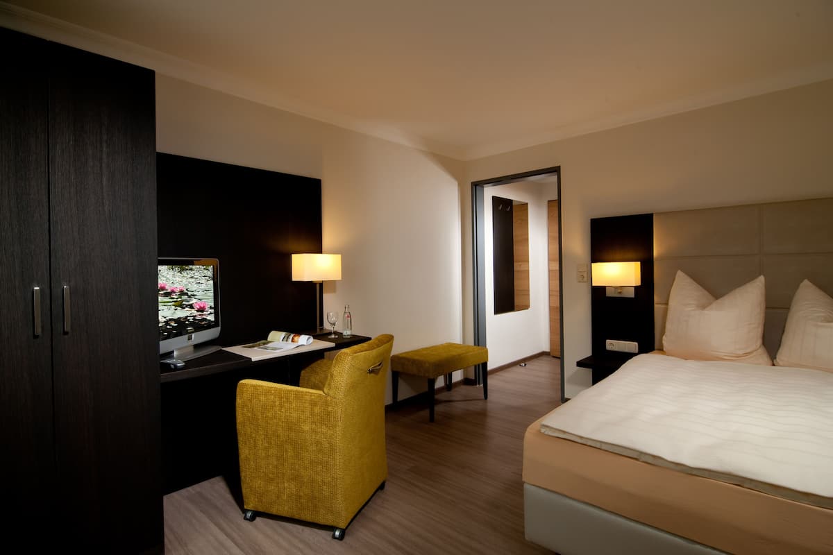 A hotel room with a bed, a desk with a computer monitor, a chair, a small table, and two bedside lamps.