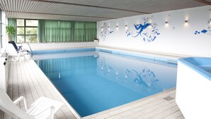 Een binnenzwembad met helderblauw water, een betegelde vloer en een witte muur met blauwe bloemdecoraties. Er staan loungestoelen langs het zwembad.