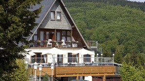Een chalet met een houten balkon, zitplaatsen buiten en een berg op de achtergrond.