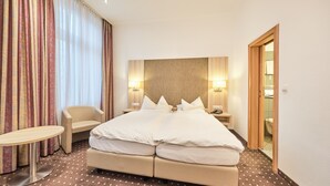 Una habitación de hotel con una cama, mesitas de noche, una silla y una pequeña mesa.