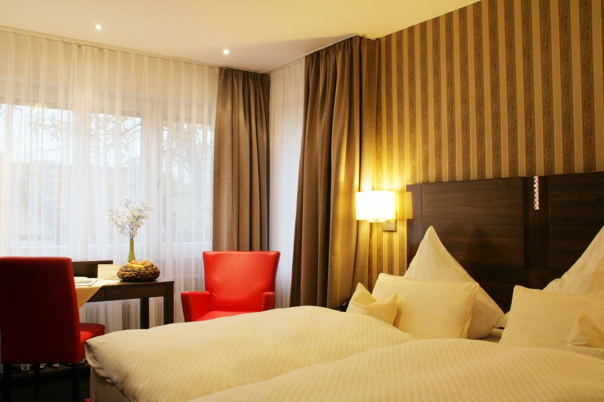 A hotel room with two beds, a desk with a chair, and a lamp.