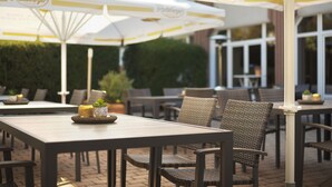 Un espace extérieur aménagé avec des tables et des chaises sous des parasols à rayures, un pot de fleurs et un sol en briques.
