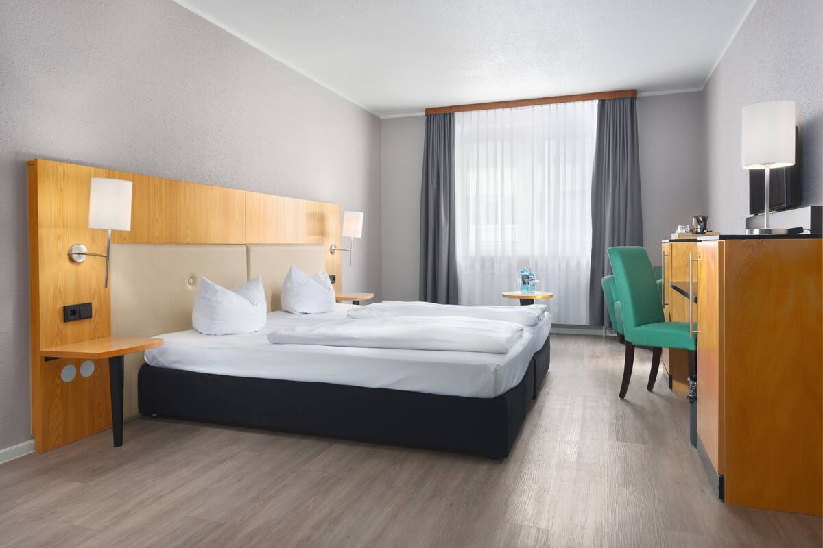 Une chambre d’hôtel avec deux lits, un bureau, une chaise, une télévision et une fenêtre avec des rideaux.