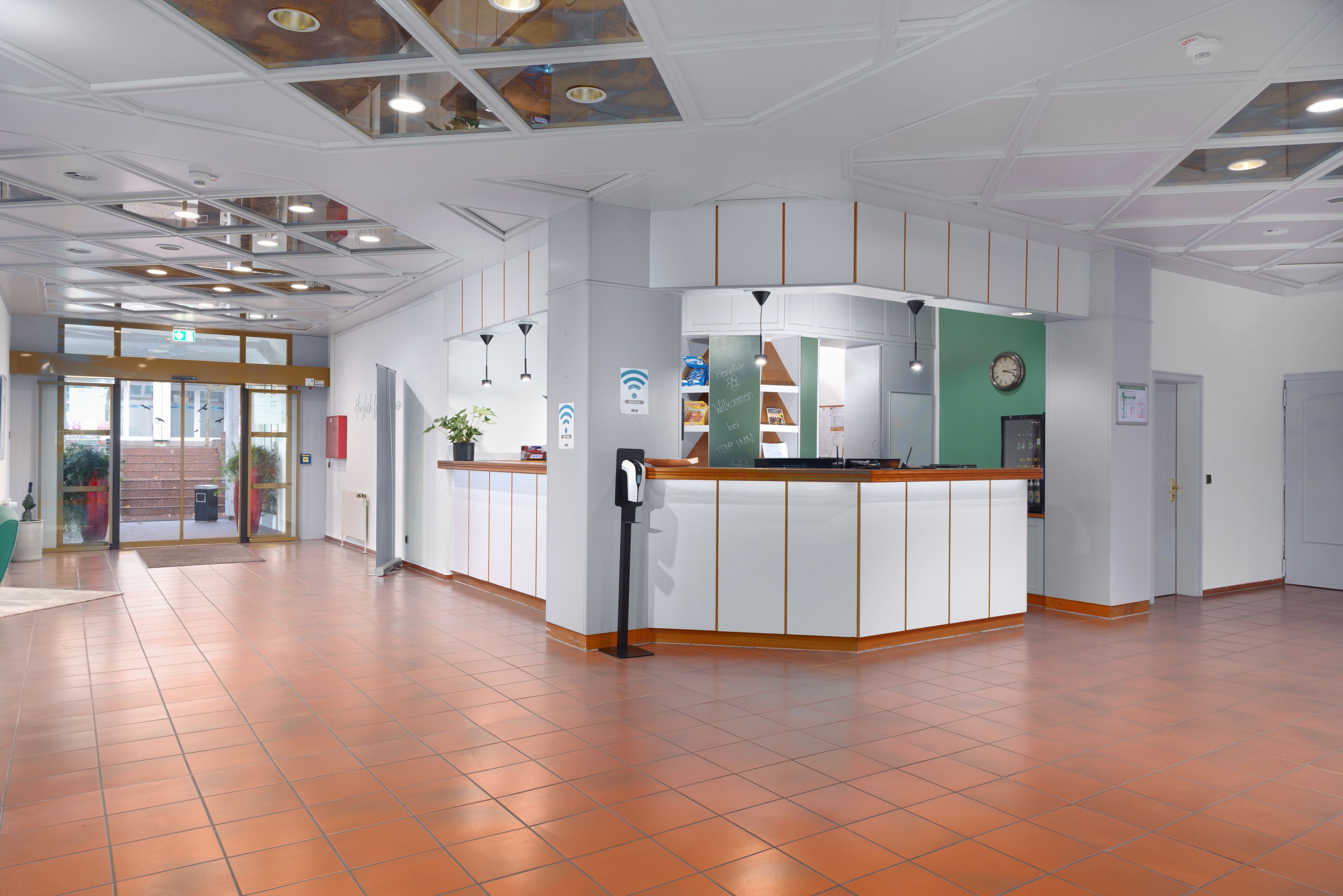 A spacious lobby with a reception desk, a green wall with a clock, and a tiled floor.