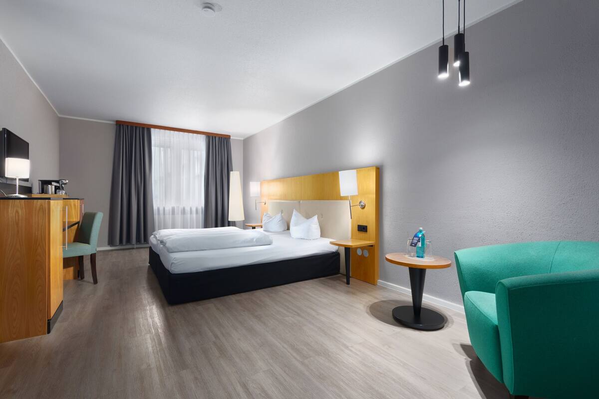 Une chambre d’hôtel comprenant un lit, un bureau, une chaise, une petite table et une lampe.