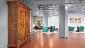 Un hall d’entrée spacieux, avec un grand meuble en bois, des fauteuils de couleur turquoise et un sol carrelé.